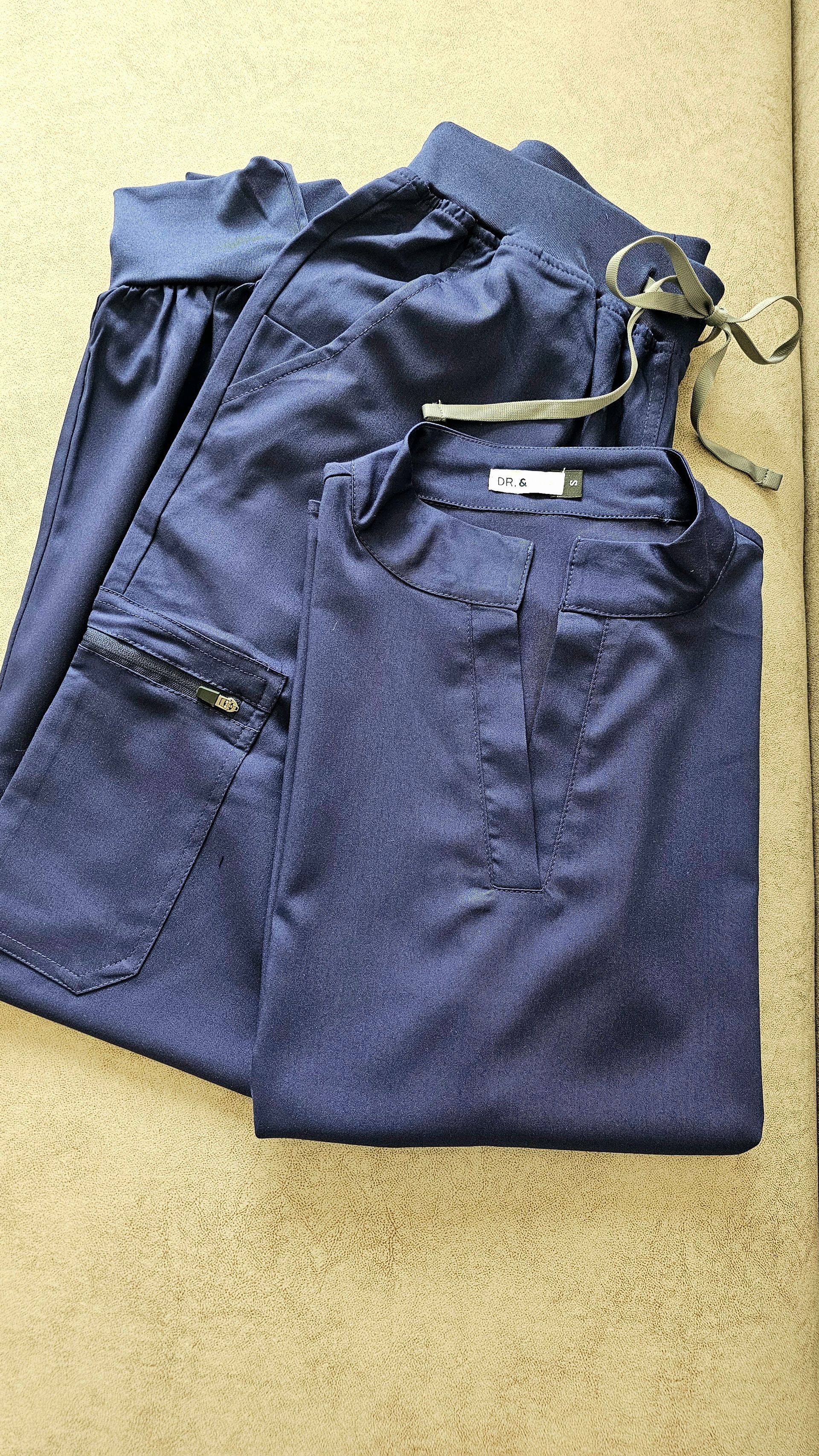 Tres mujeres con uniformes médicos, azul marino, negro y burdeos, de pie en un edificio moderno, sonriendo.