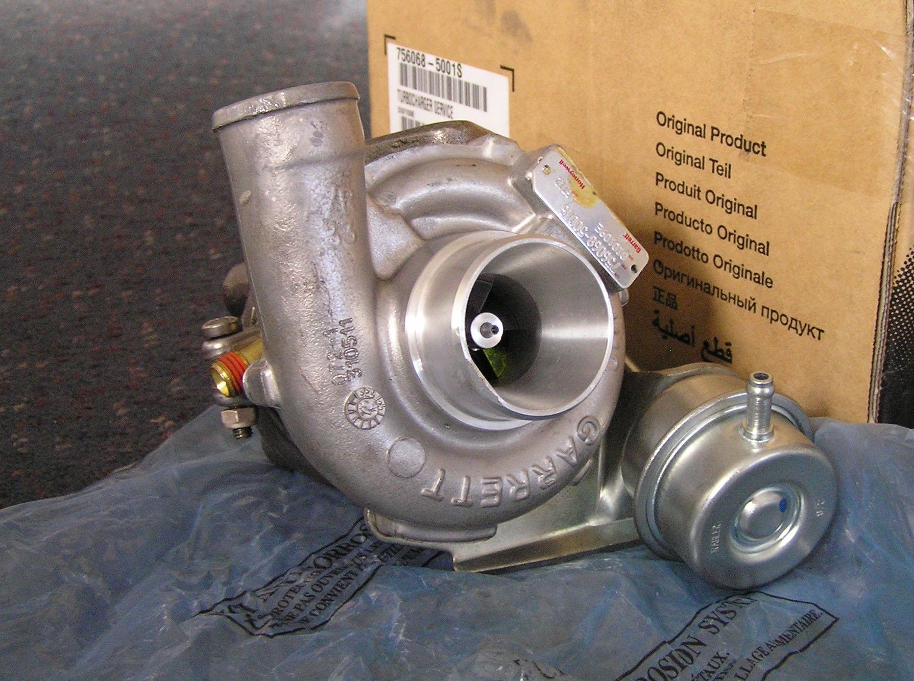 A drag racer stands next to his white race car on a track. The car has a cloth over its front and a yellow logo.