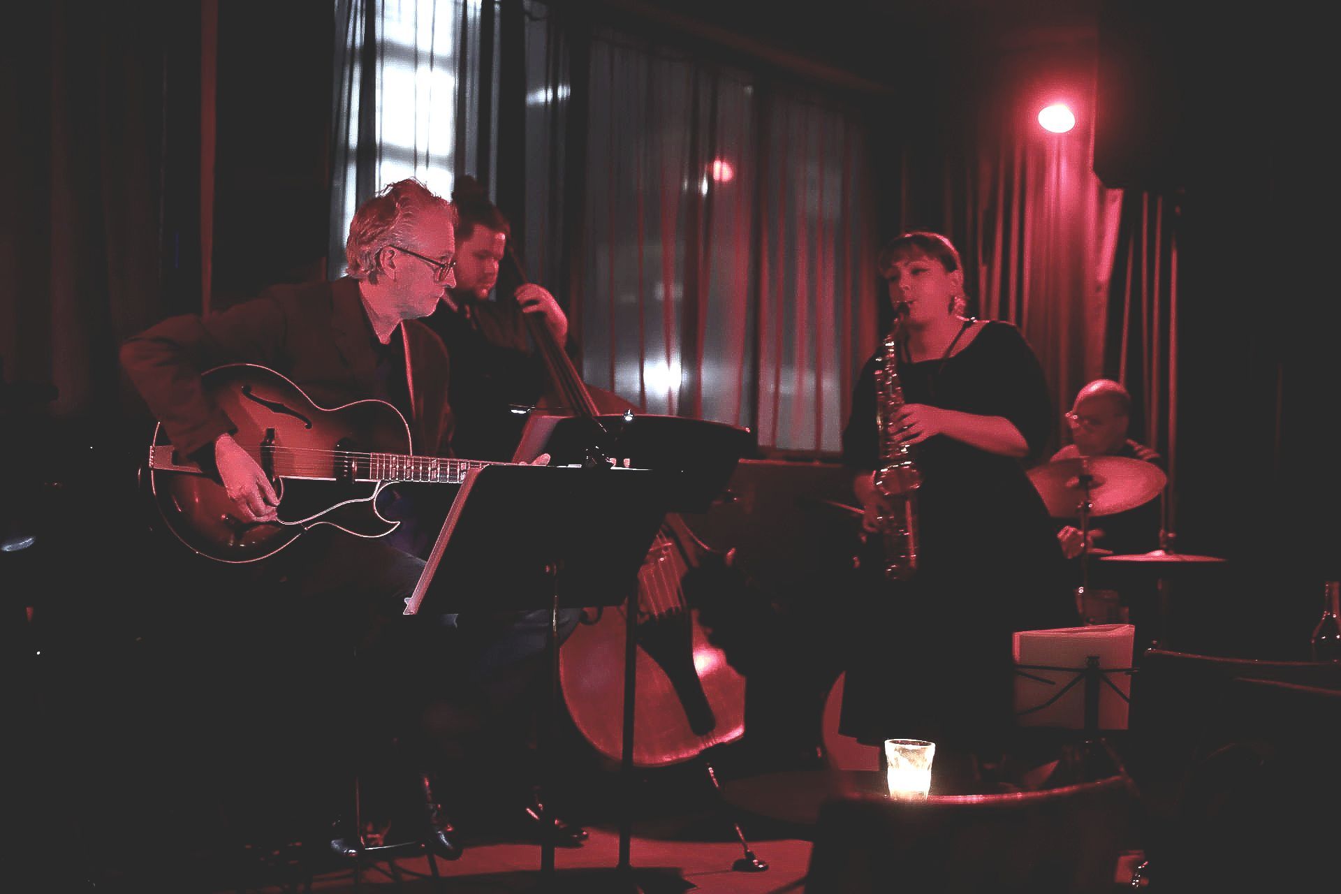 A man is playing a guitar and a woman is playing a saxophone in a dark room.