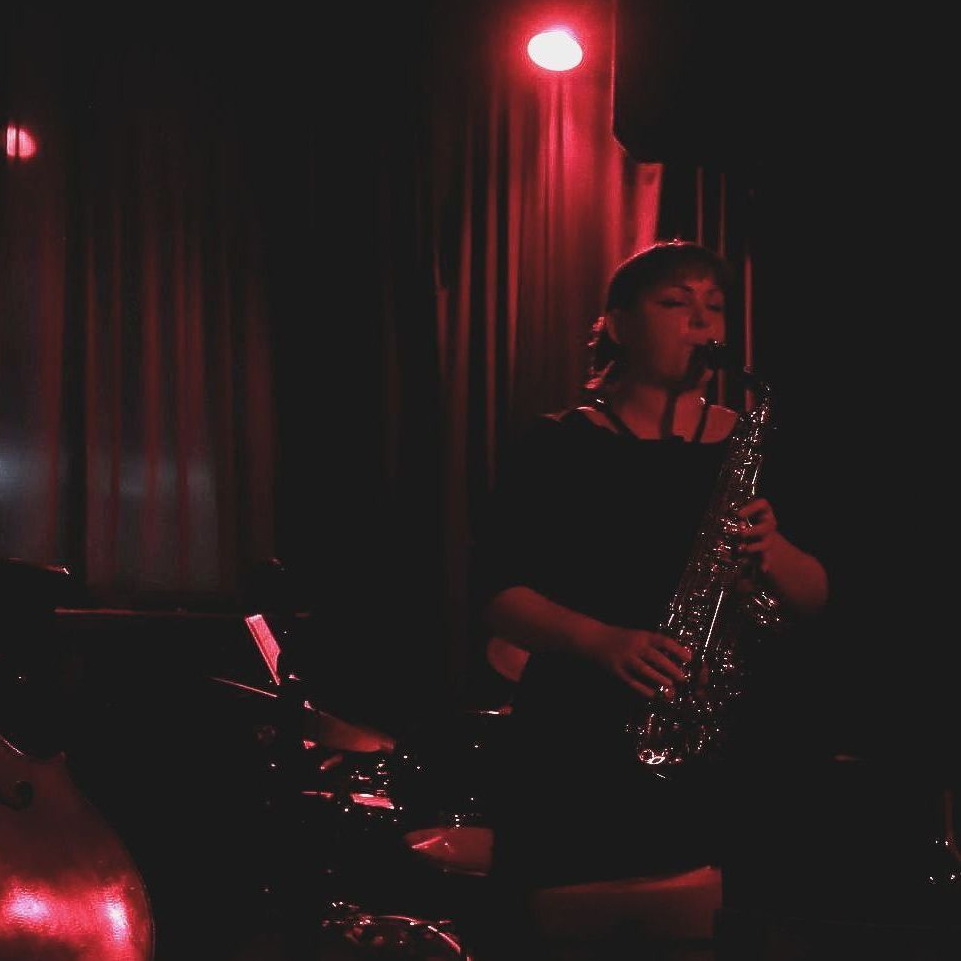 Woman playing saxophone on stage under red light.
