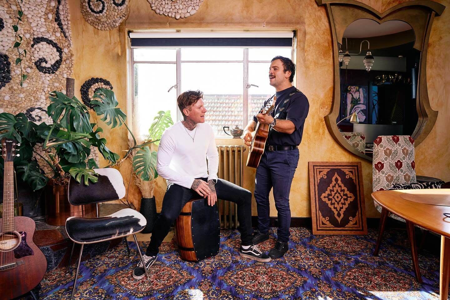 Two men are playing guitars in a living room.