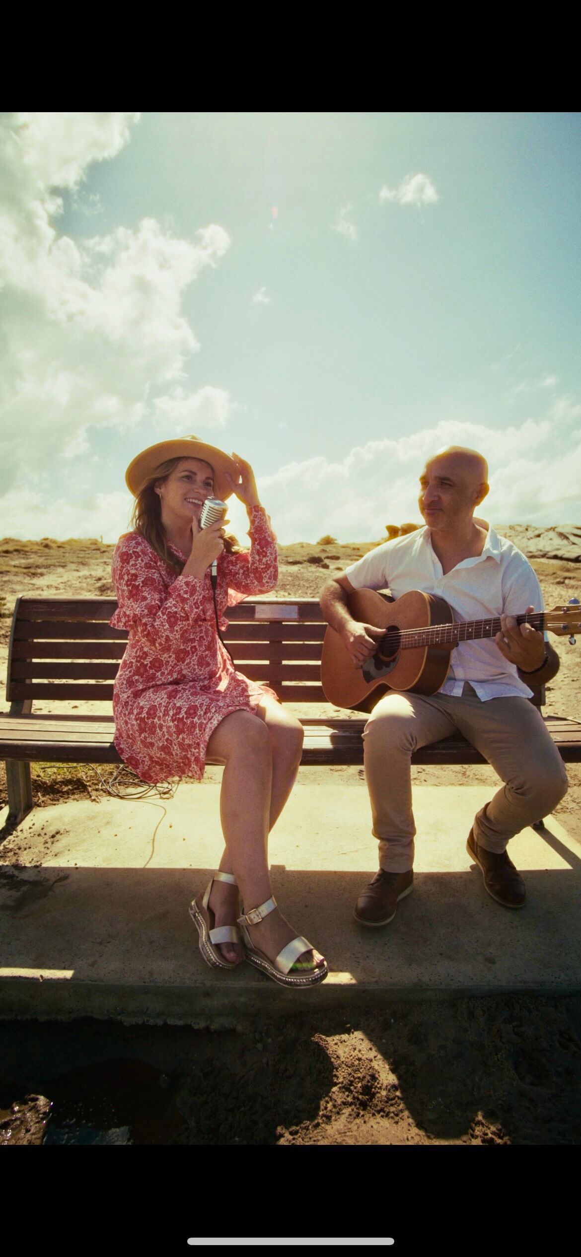 A man is playing a guitar and a woman is sitting on a bench.