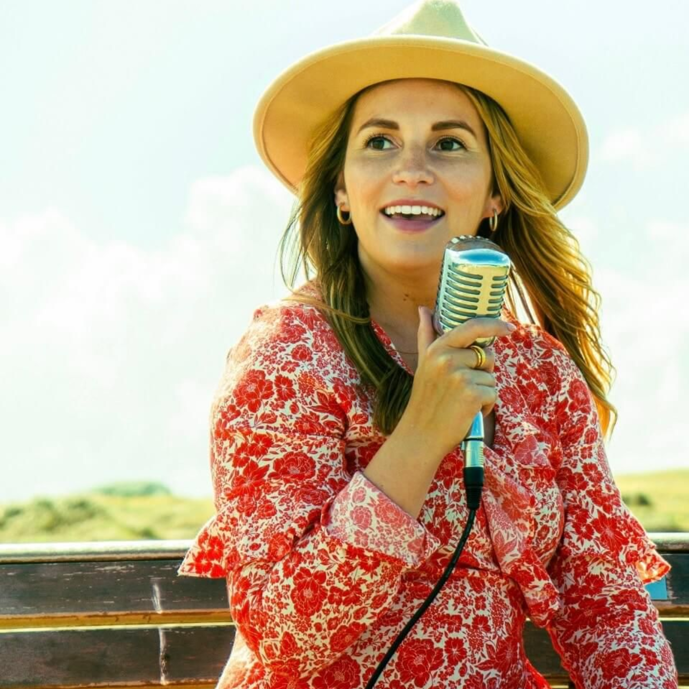 Woman singing, man playing guitar on rocky shore, ocean and blue sky in background.