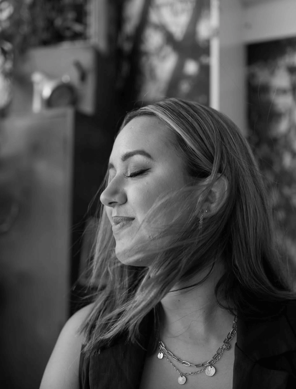 A black and white photo of a woman with her eyes closed and her hair blowing in the wind.