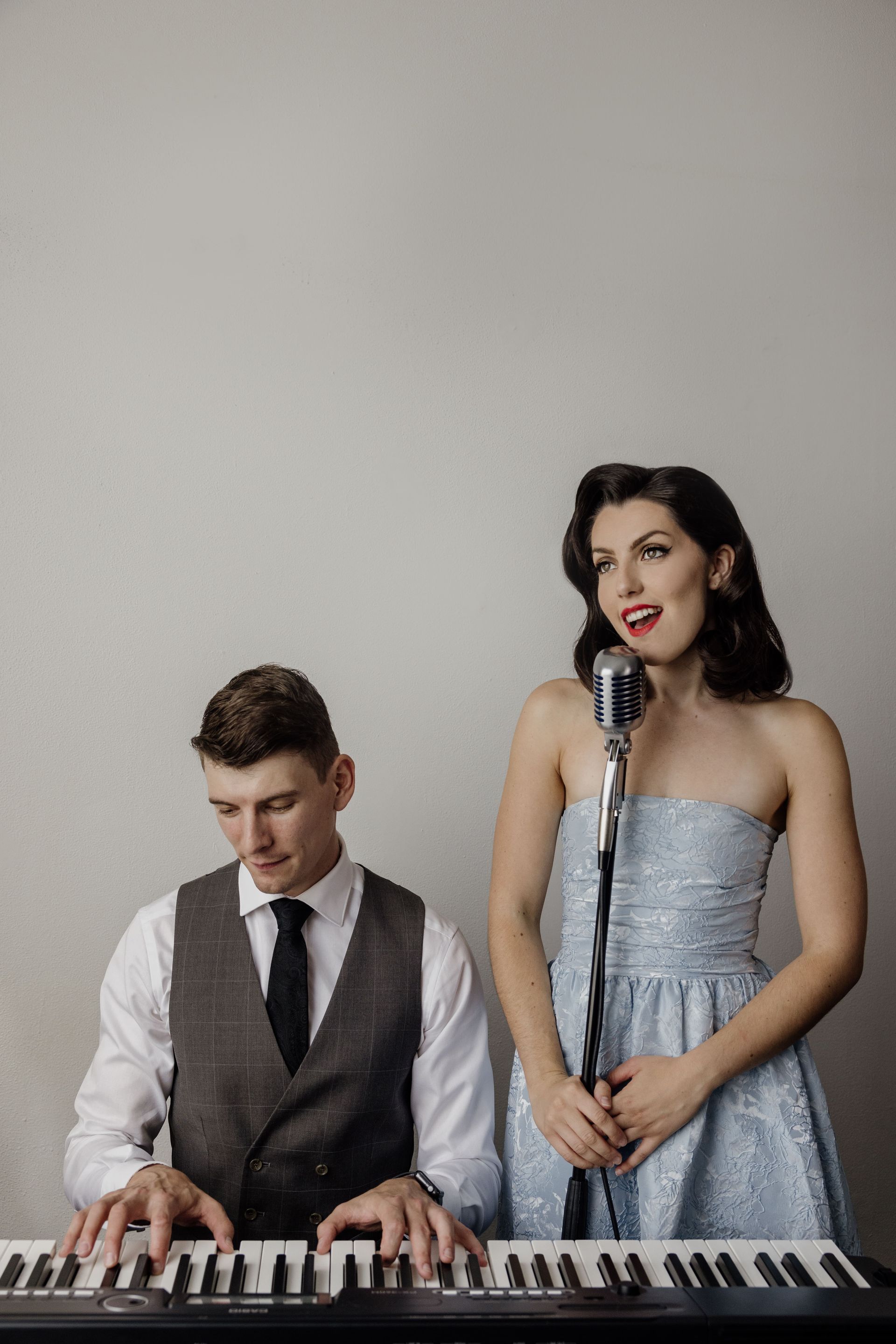 A man is playing a piano and a woman is singing into a microphone.