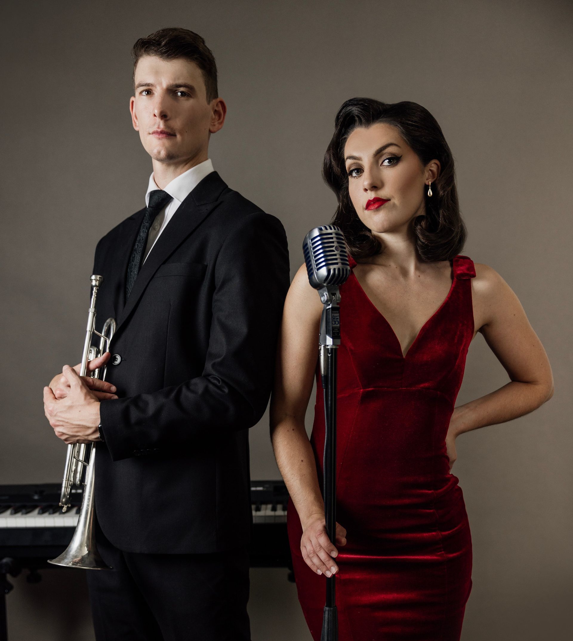 A man in a suit and tie is holding a trumpet and a woman in a red dress is holding a microphone.