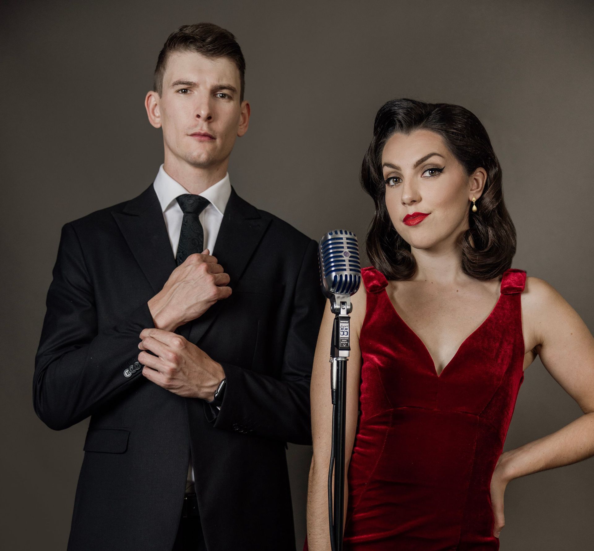 A man in a suit and tie and a woman in a red dress are standing next to microphones