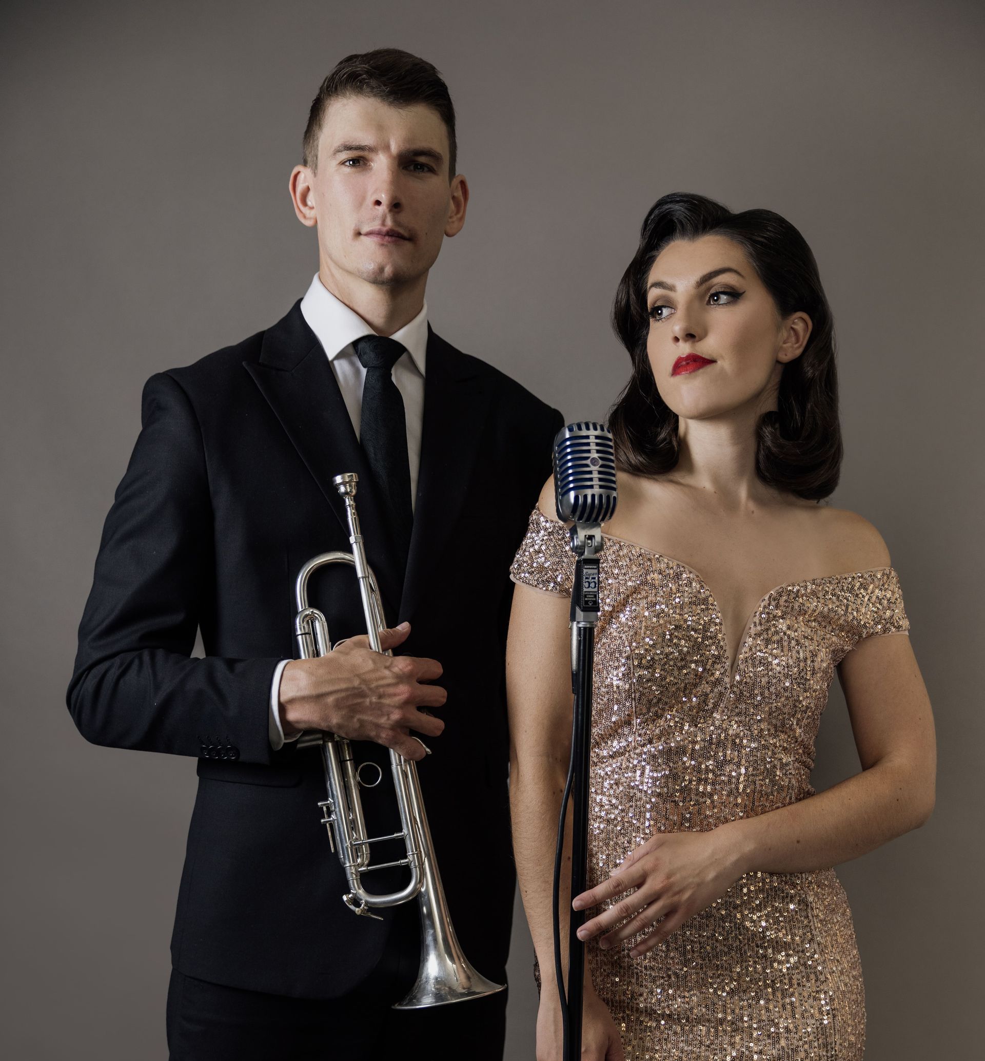A man in a suit is holding a trumpet next to a woman in a gold dress.
