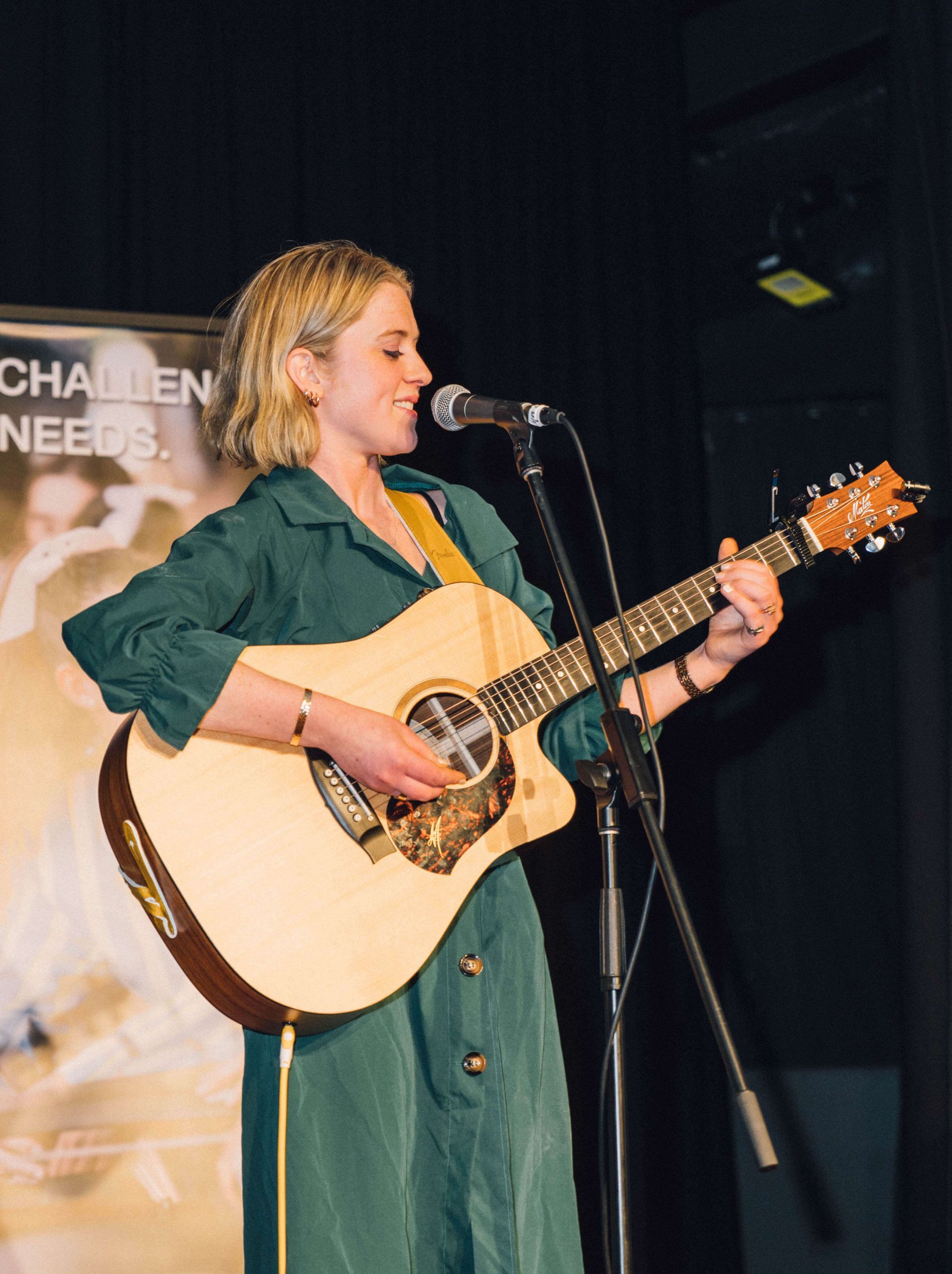 A woman in a green dress is playing a guitar and singing into a microphone.