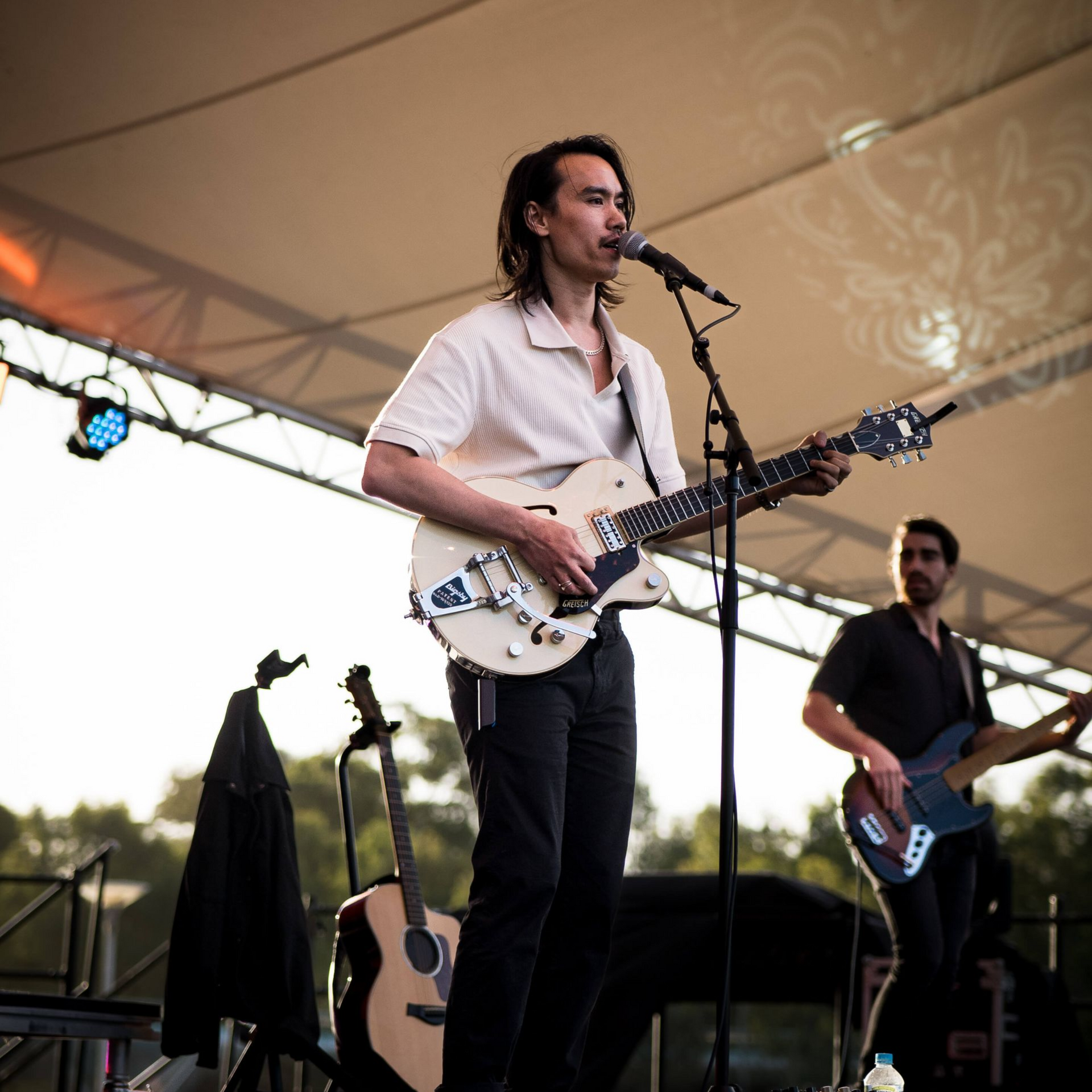 Man playing guitar and singing on stage; another man on bass in background.