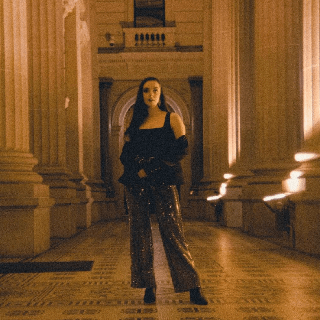 A woman in a black dress is standing in a hallway with columns.