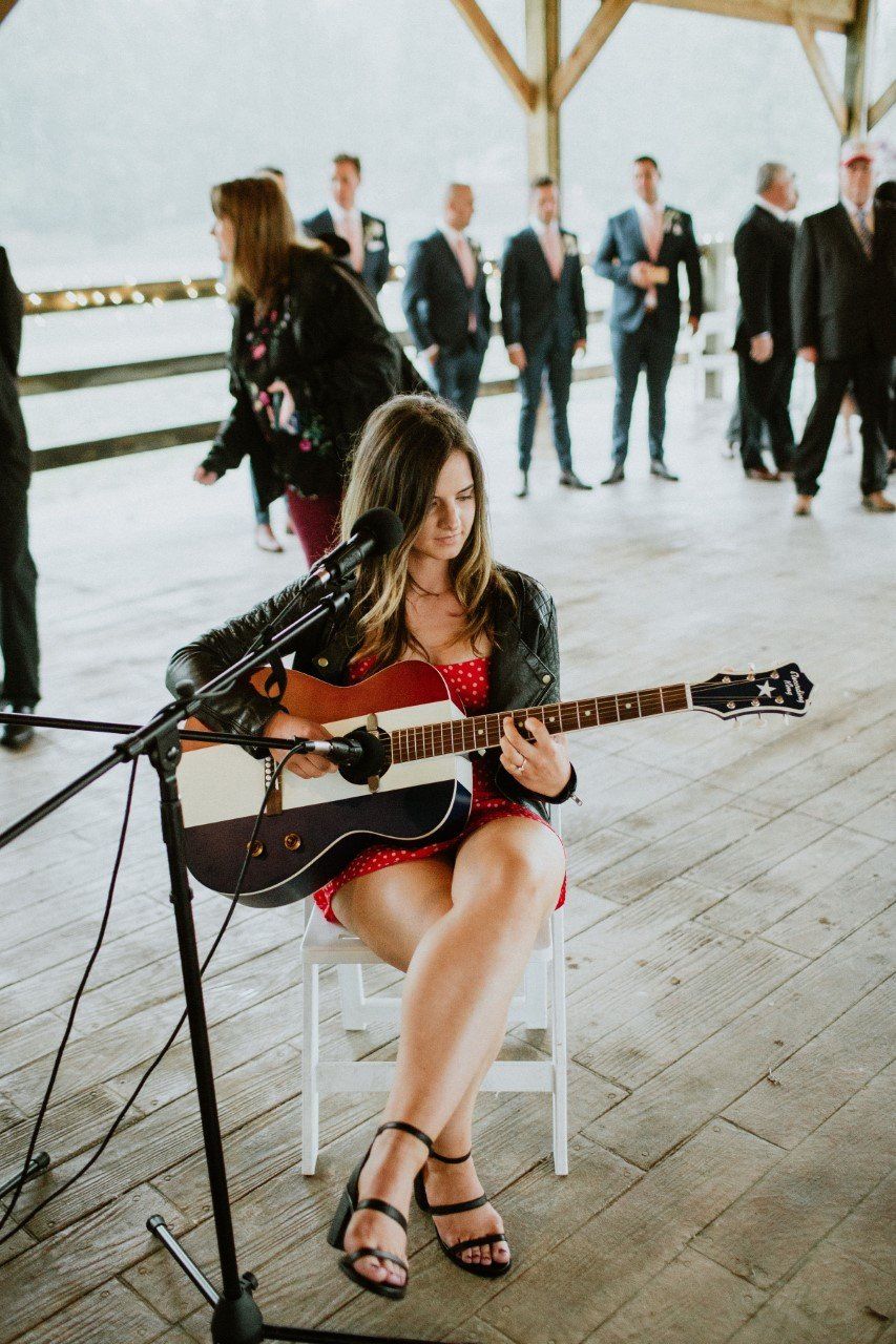 A woman is sitting in a chair playing a guitar in front of a microphone.