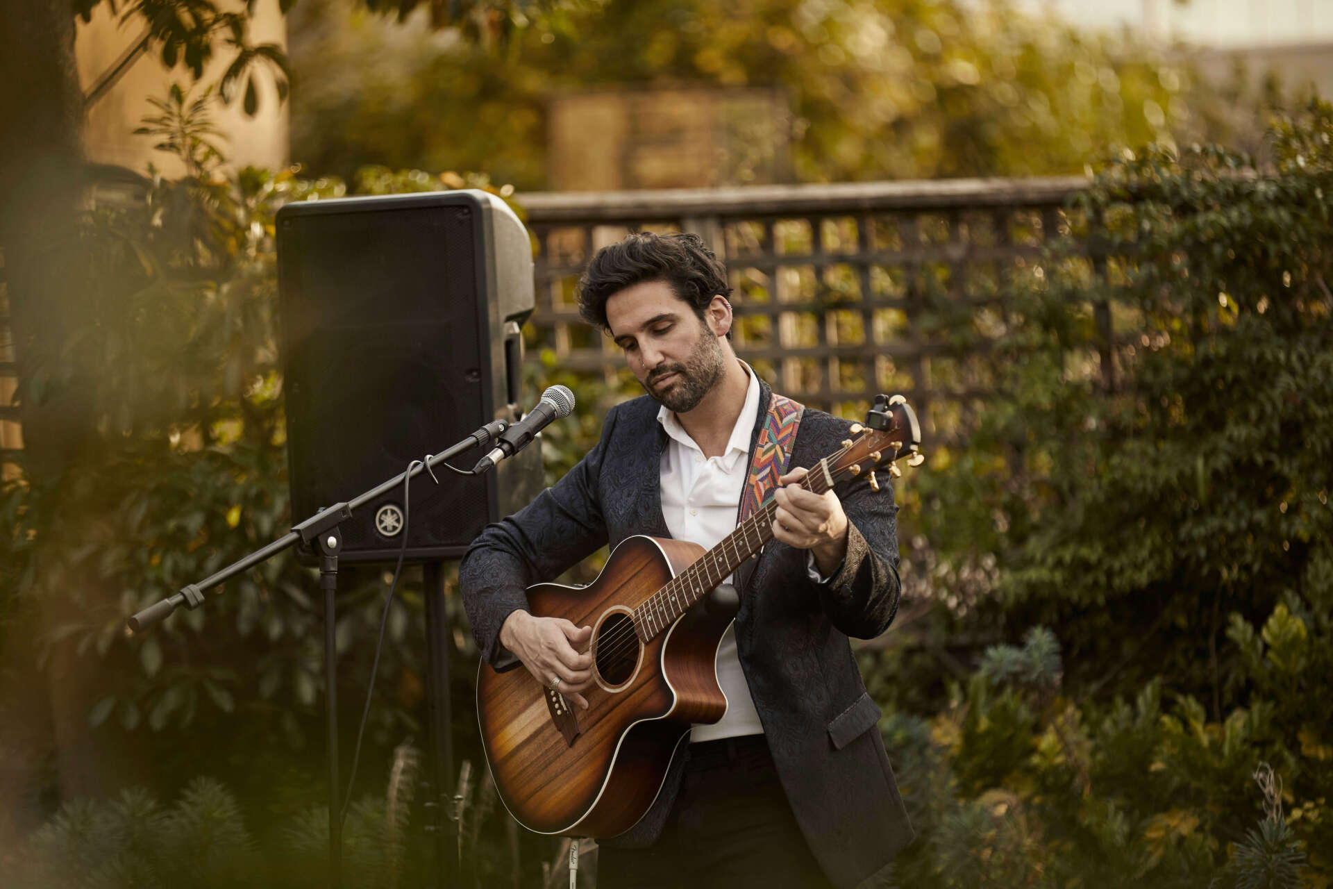 A man in a suit is playing an acoustic guitar in front of a microphone.