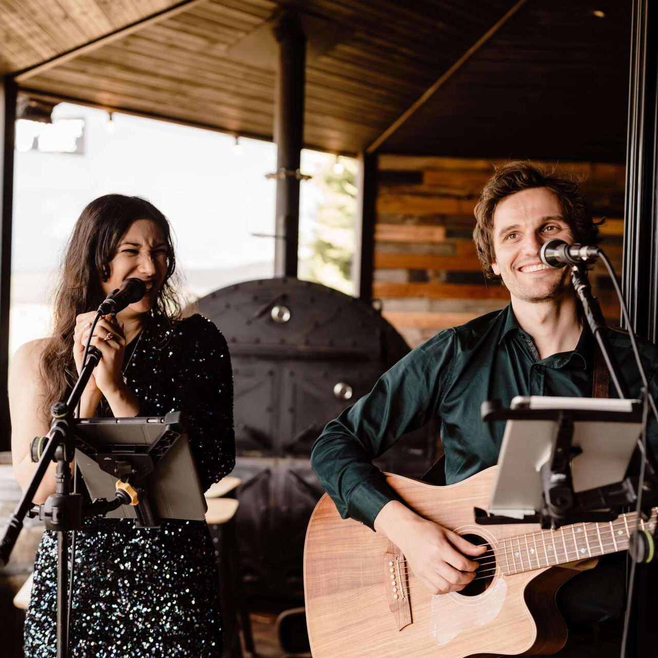 A man is playing a guitar and a woman is singing into microphones.