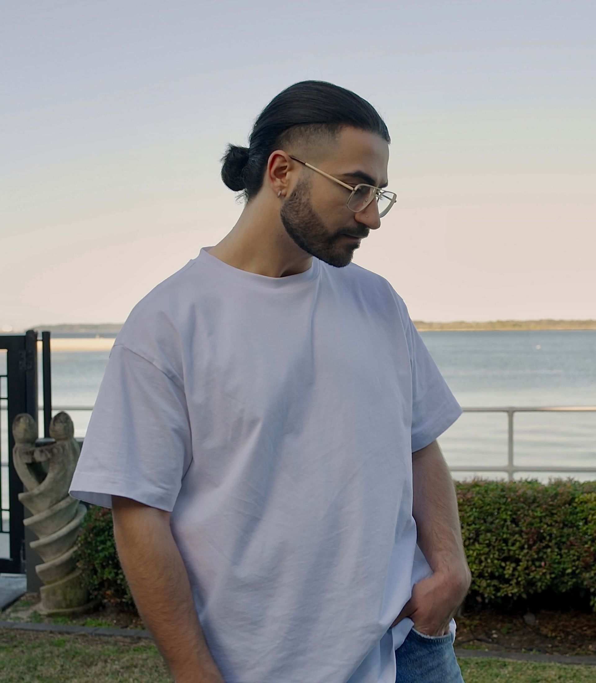 A man wearing glasses and a white t-shirt is standing in front of the ocean.