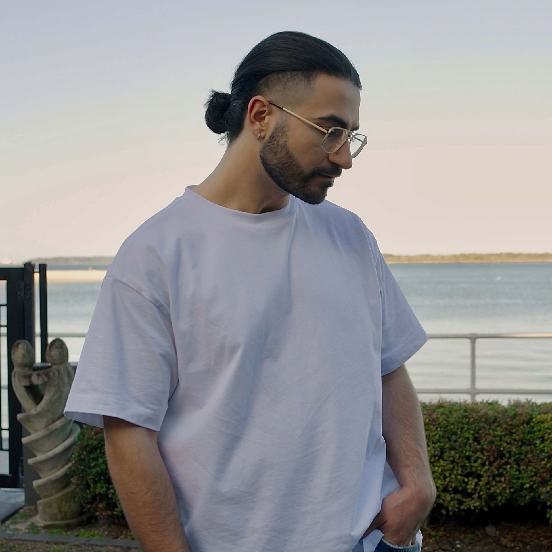 A man wearing glasses and a white shirt is standing in front of the ocean.