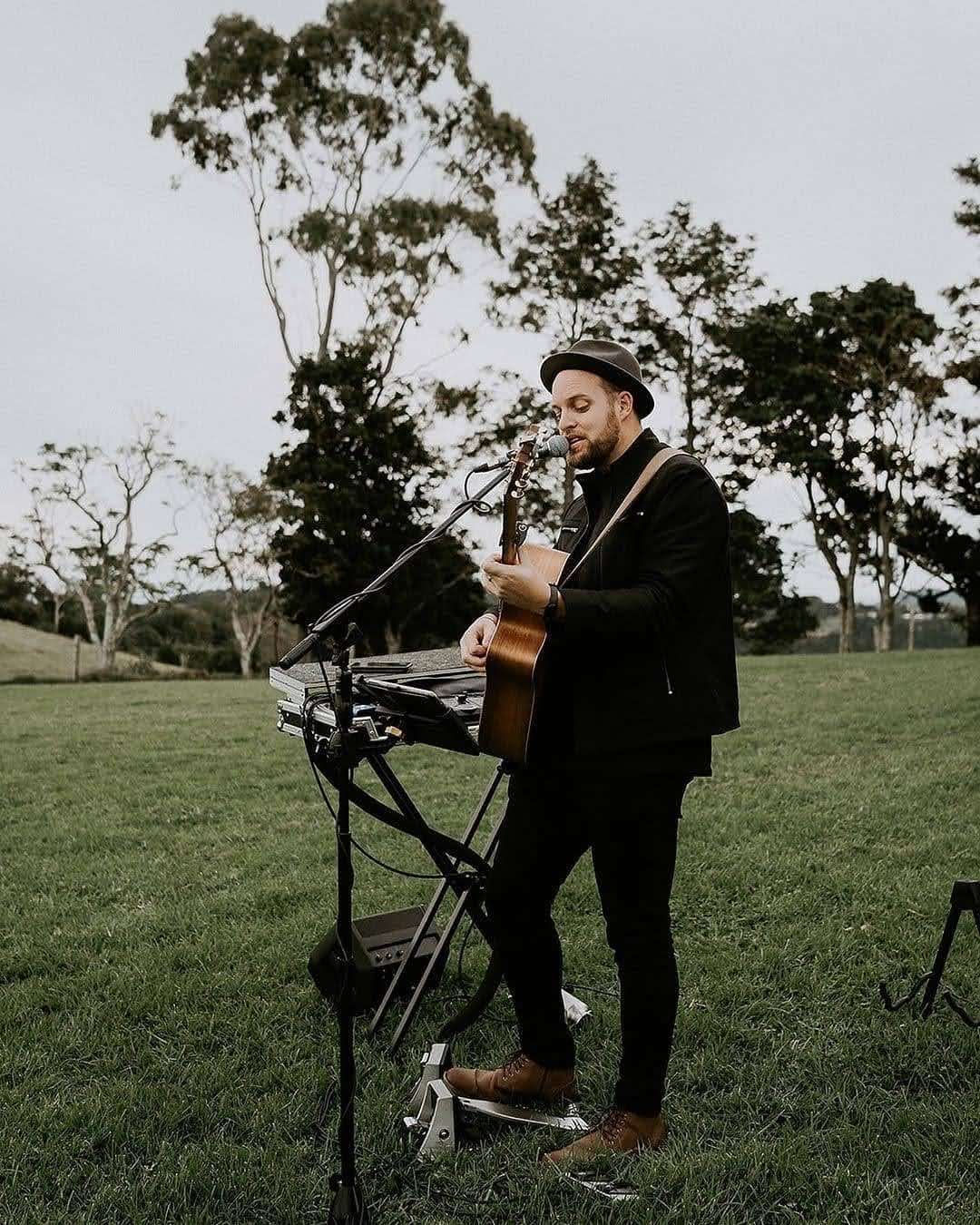 A person wearing a hat smiles and makes a peace sign while DJing at a console with a laptop, lights, and audio equipment.