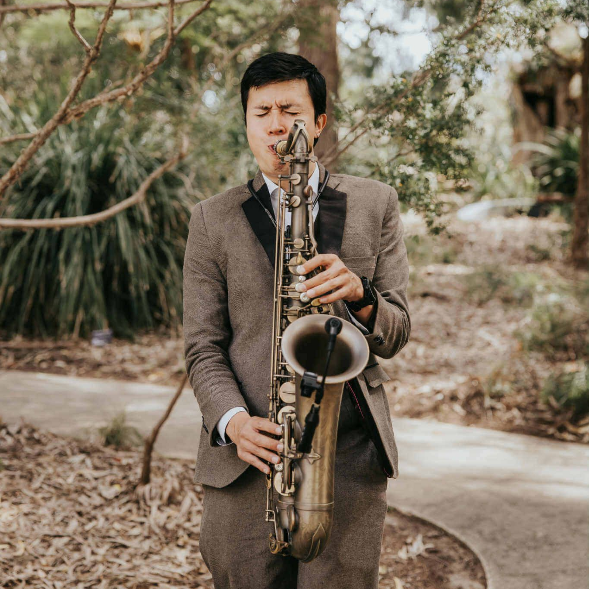 Ernesto playing saxophone outdoors, wearing a suit, eyes closed.
