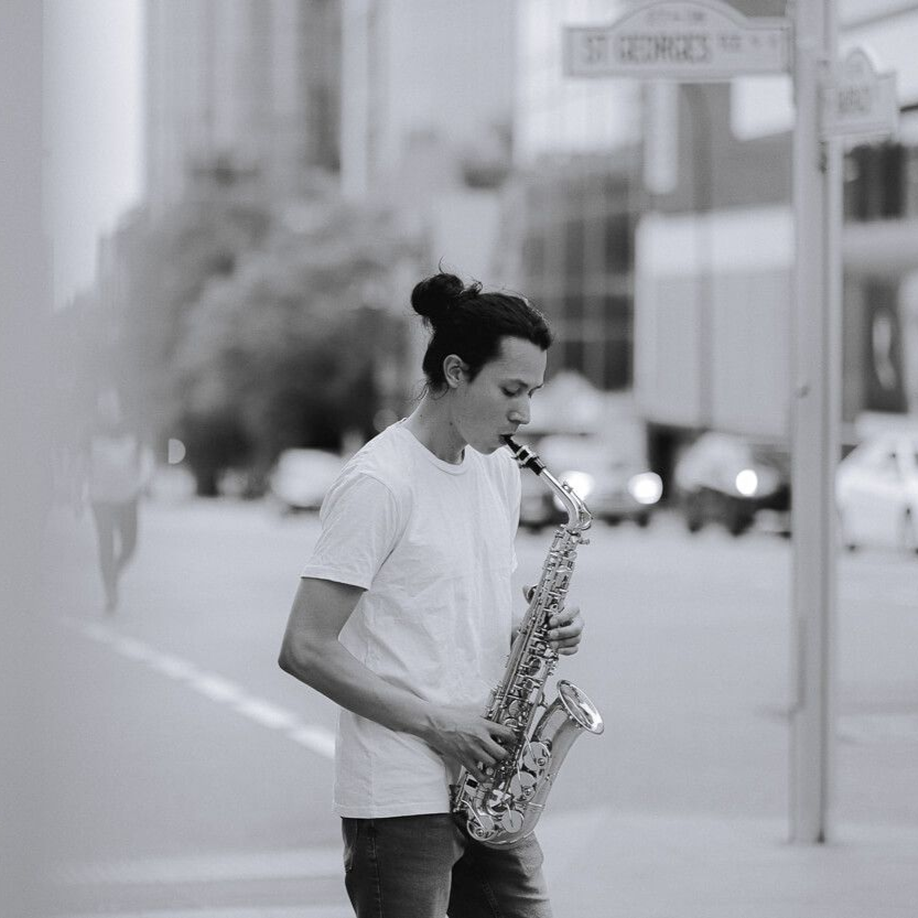 Ernesto playing a saxophone on a city street. Black and white photo.