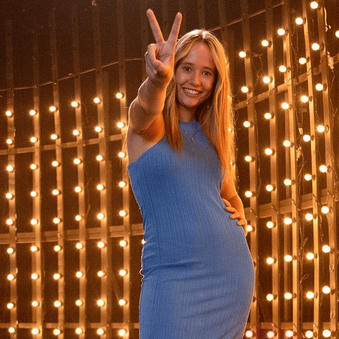 A woman in a blue dress is giving a peace sign