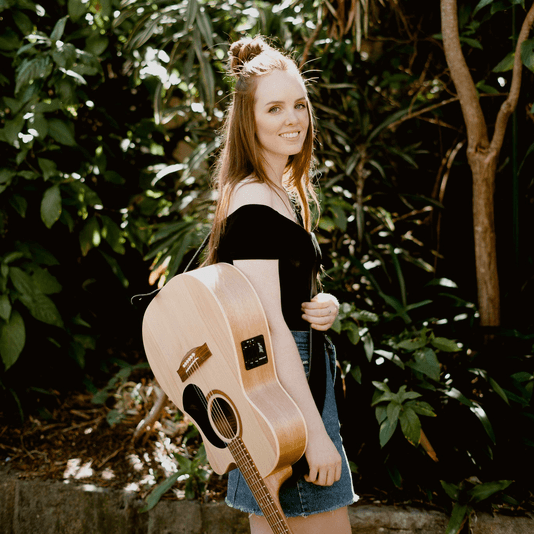 A woman is holding an acoustic guitar behind her back.