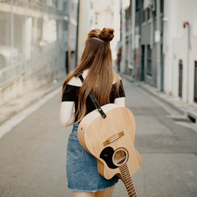 A woman is carrying an acoustic guitar on her back.