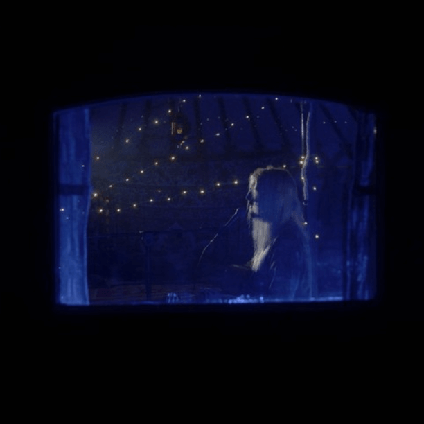 Woman playing piano, silhouetted in a blue-lit window frame, surrounded by fairy lights.
