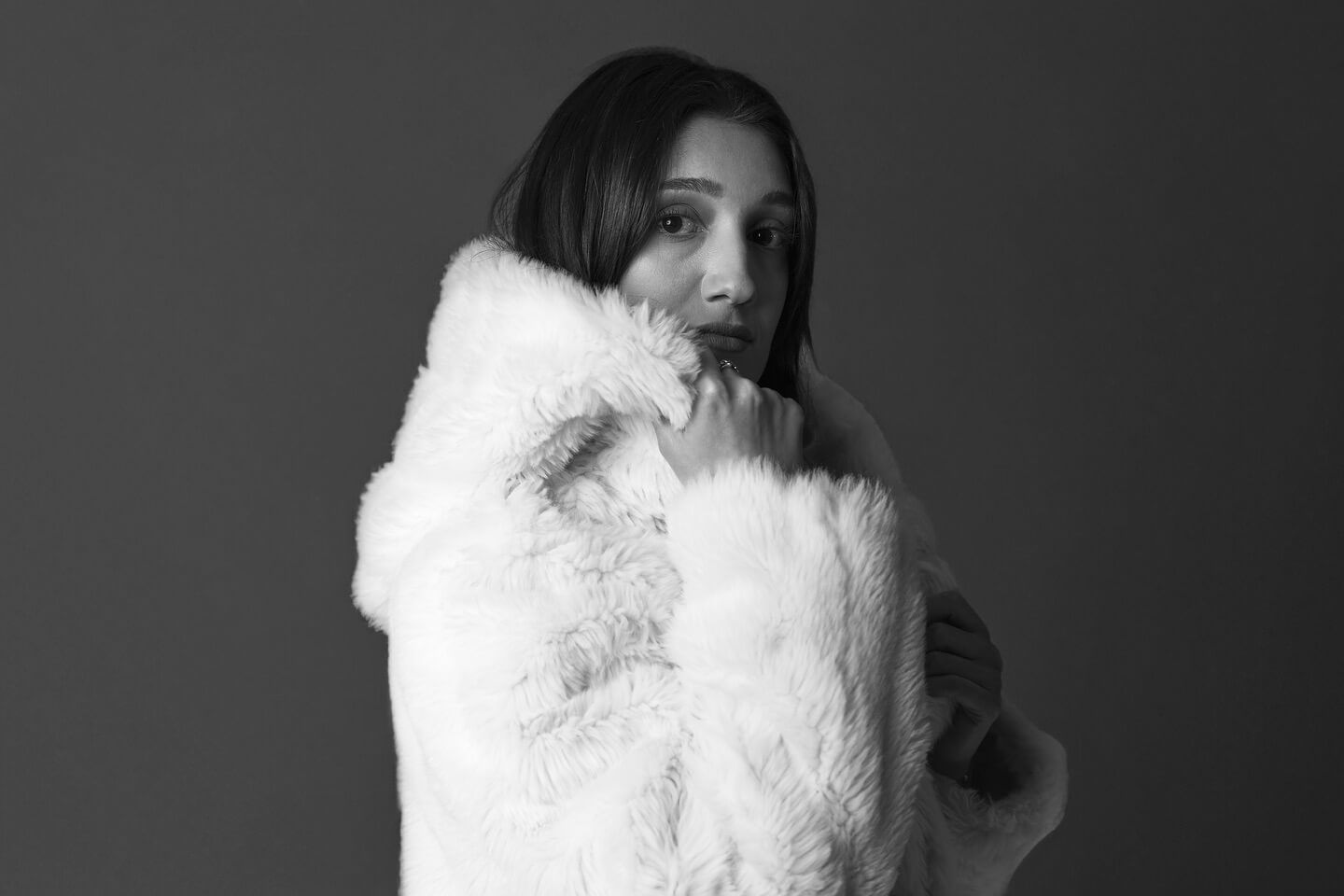 Woman in white fur coat, looking at the camera with a slightly concerned expression.