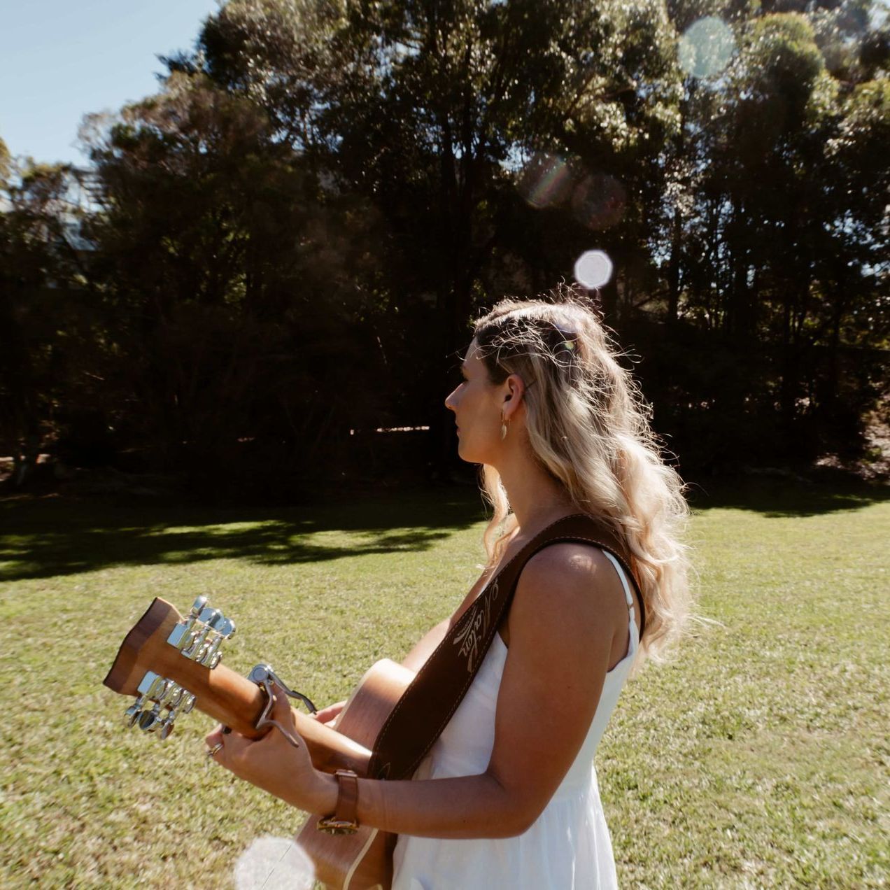 A woman in a white dress is holding a guitar in a field