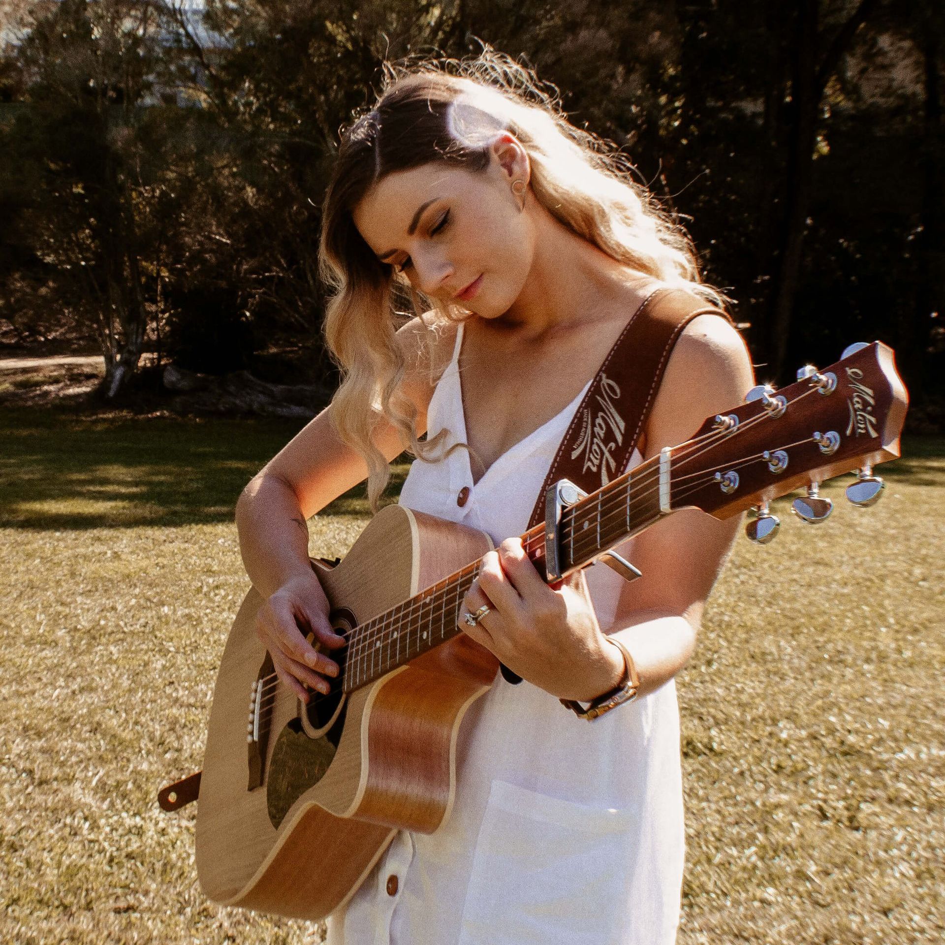 A woman in a white dress is playing an acoustic guitar