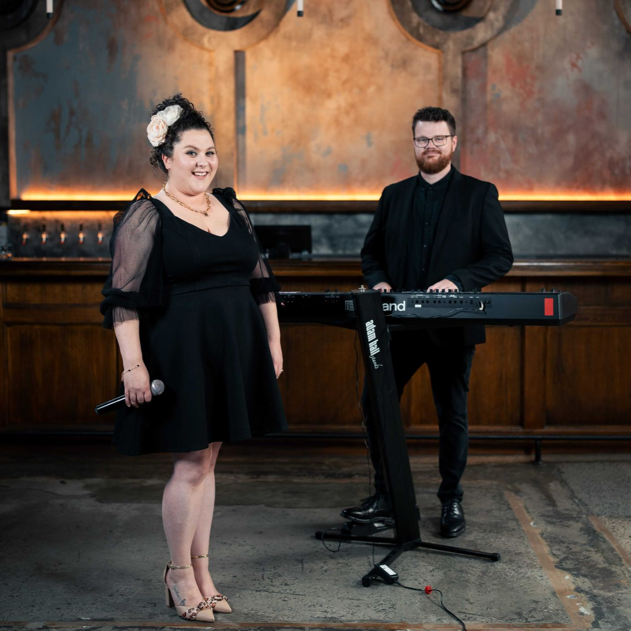 A female singer and male keyboardist perform on a stage with a dark backdrop.