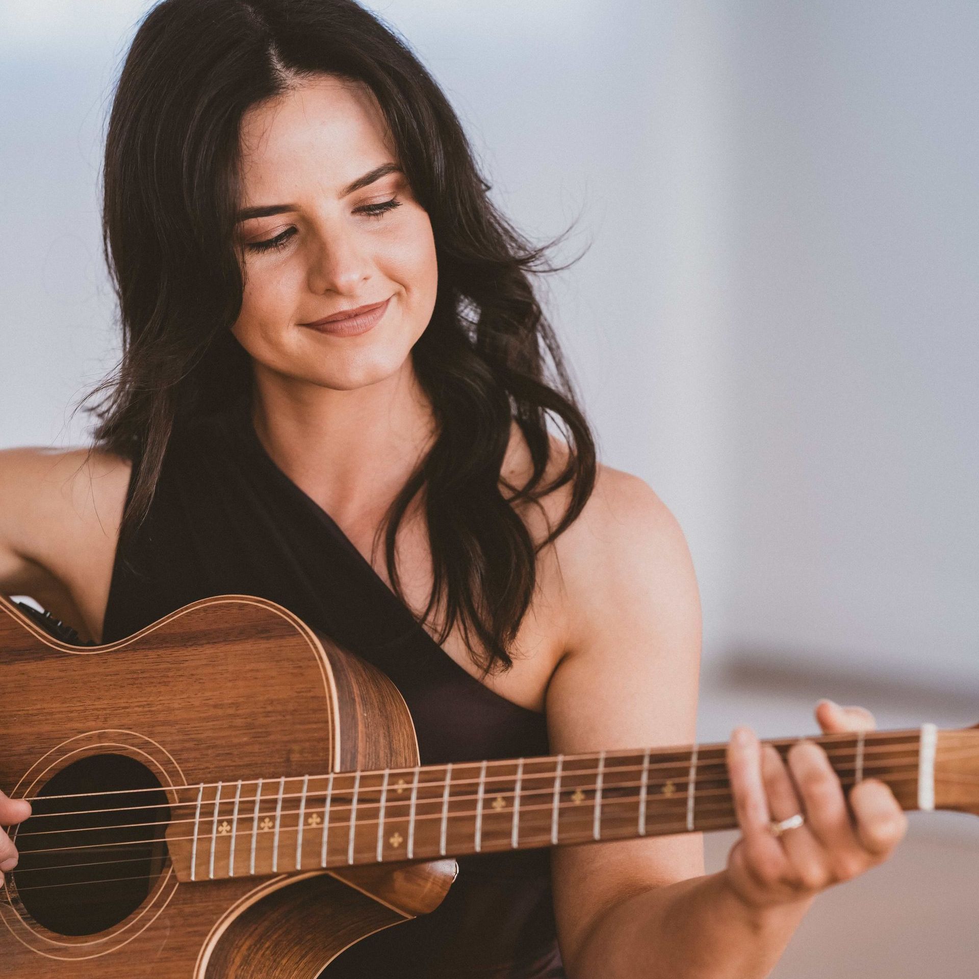 A woman in a black top is playing an acoustic guitar