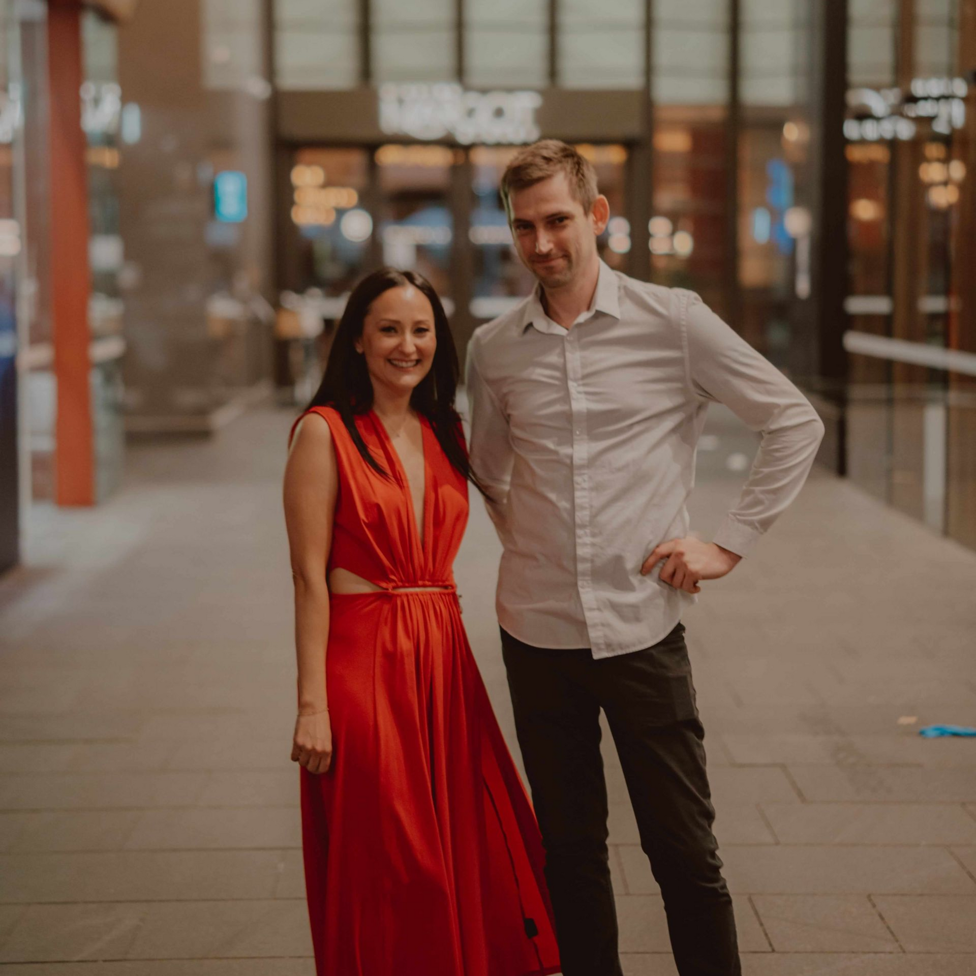 Woman in red dress and man in light shirt stand outside a building