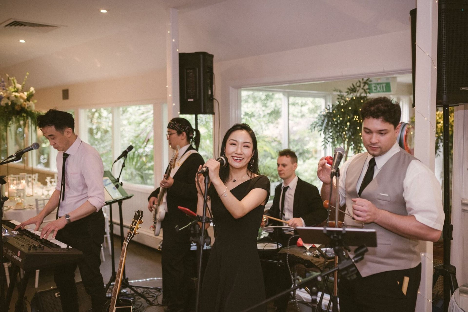 A group of people are playing instruments and singing into microphones in a room.