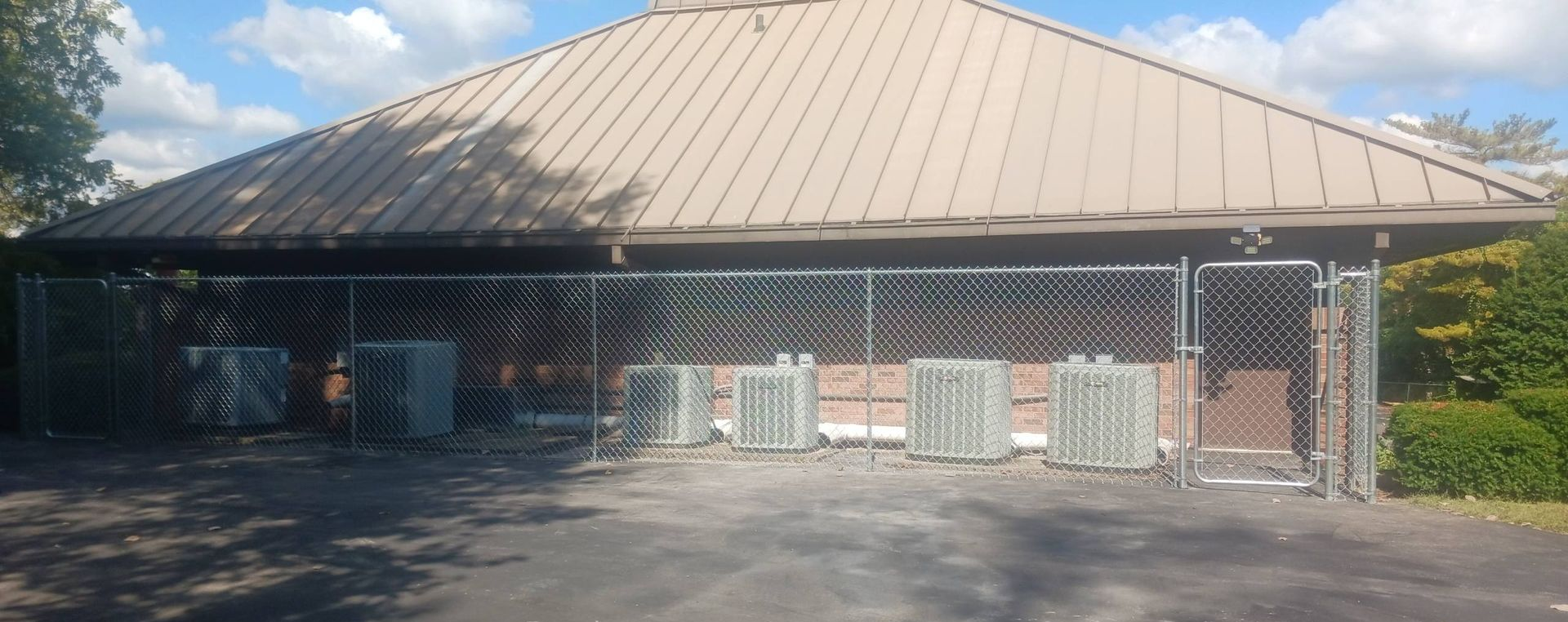 A building with a tan roof, chain-link fence, and several outdoor air conditioning units.