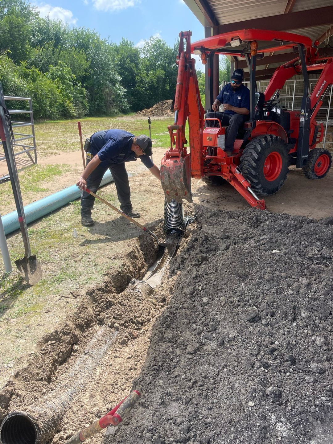 Two men are digging a hole in the ground next to a tractor.