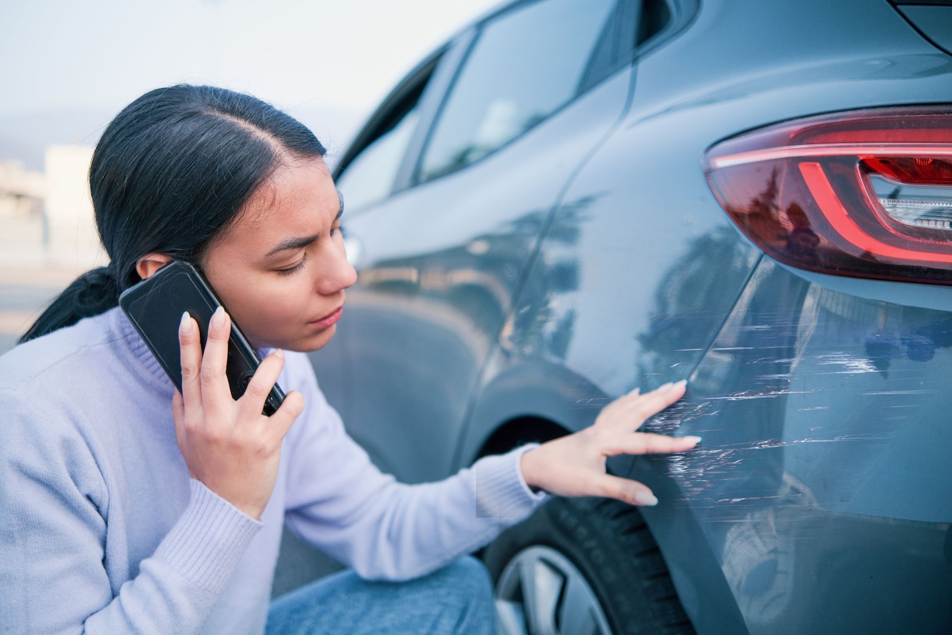 a woman is talking on a cell phone while touching a scratched car