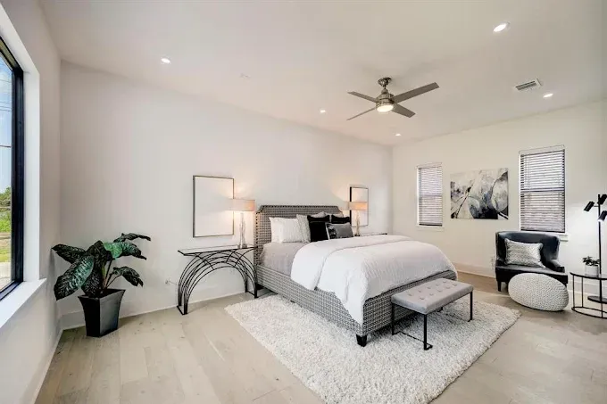 A bedroom with a bed , chair , table and ceiling fan.
