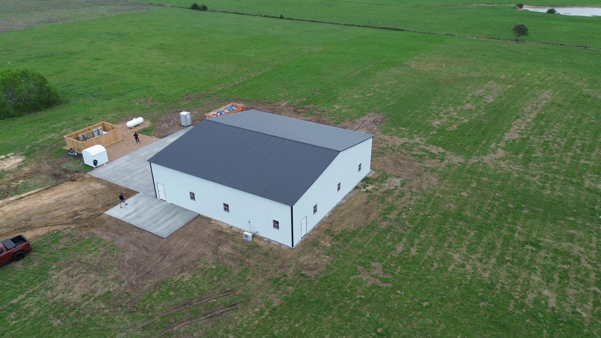 An aerial view of a large white barn in the middle of a grassy field.