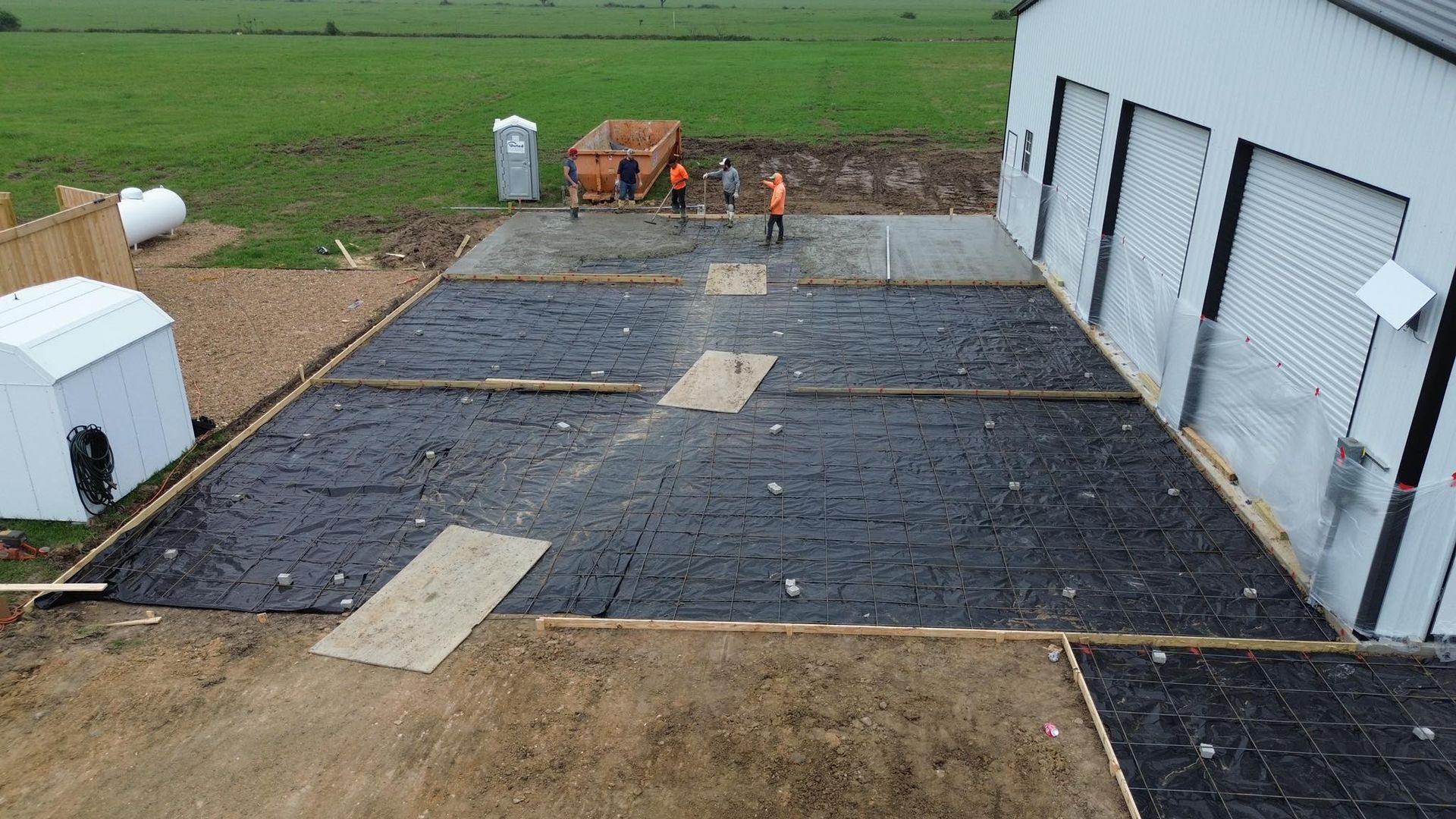 A group of people are working on a concrete driveway in front of a garage.