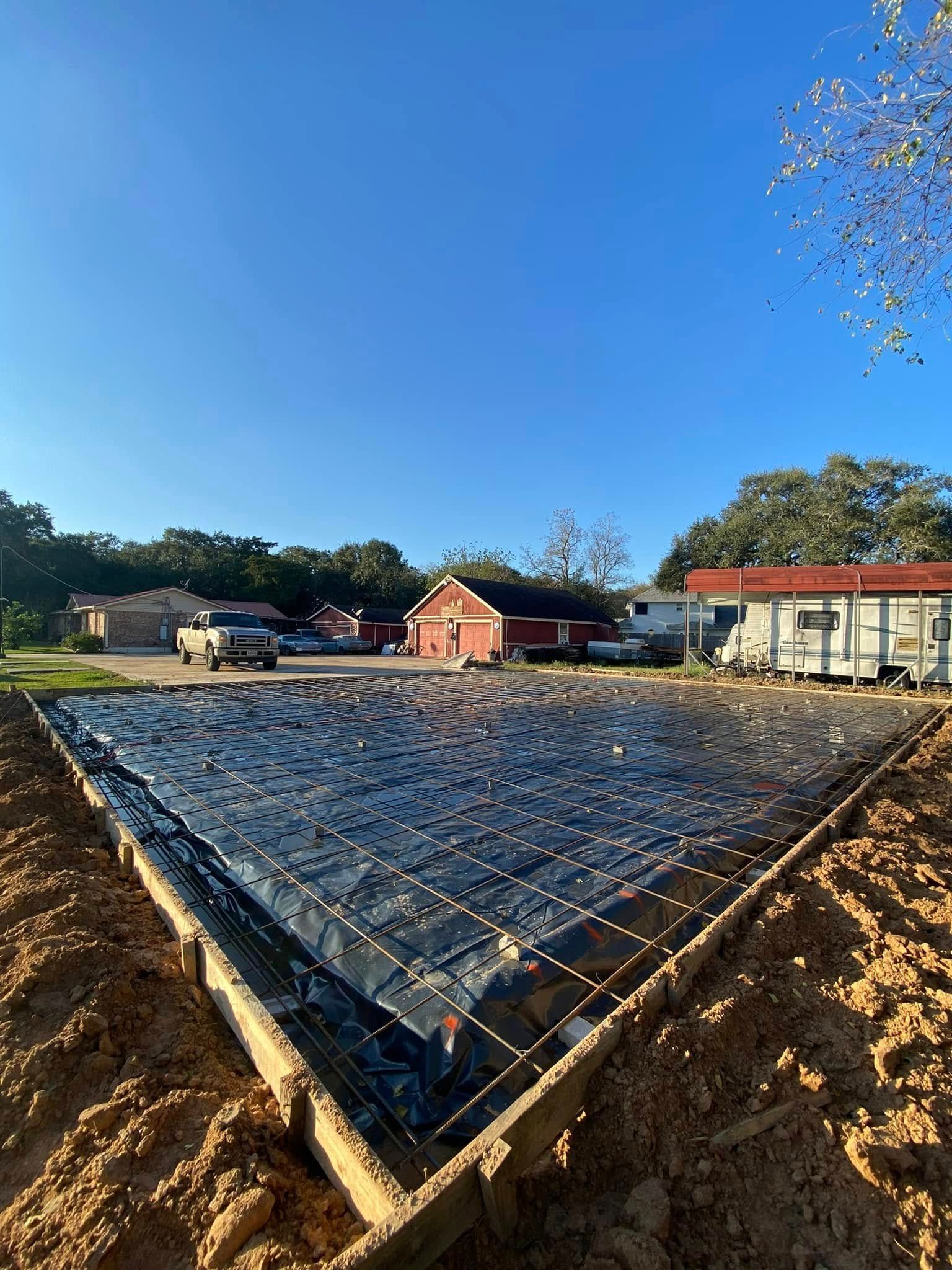 A concrete slab is being built in a dirt lot in front of a house.