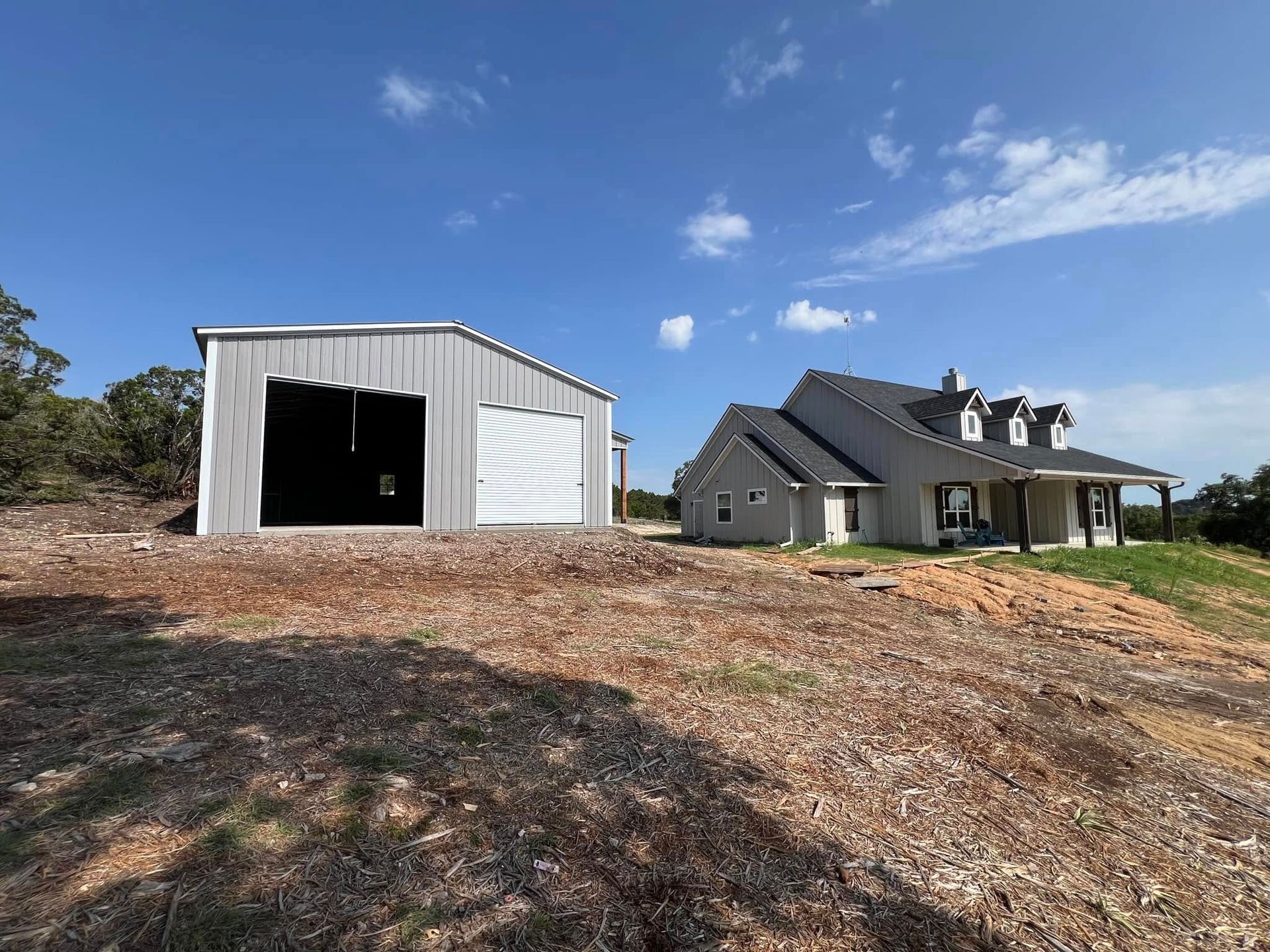 A house and a garage are sitting on top of a dirt hill.