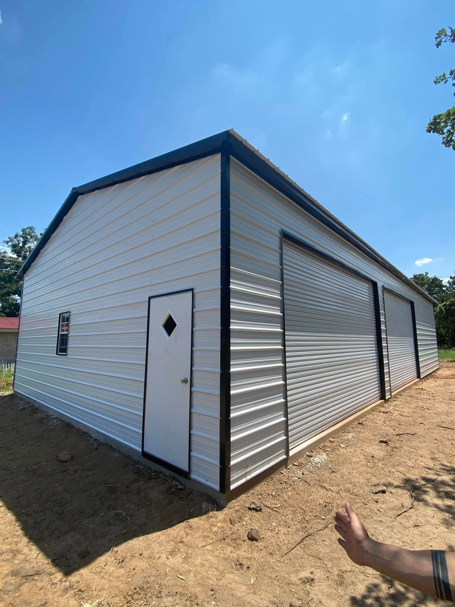 A man is standing in front of a large white metal building.
