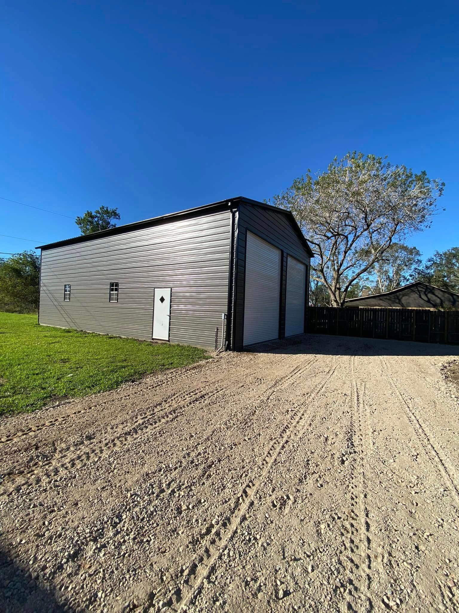 A garage is sitting on top of a gravel driveway next to a grassy field.