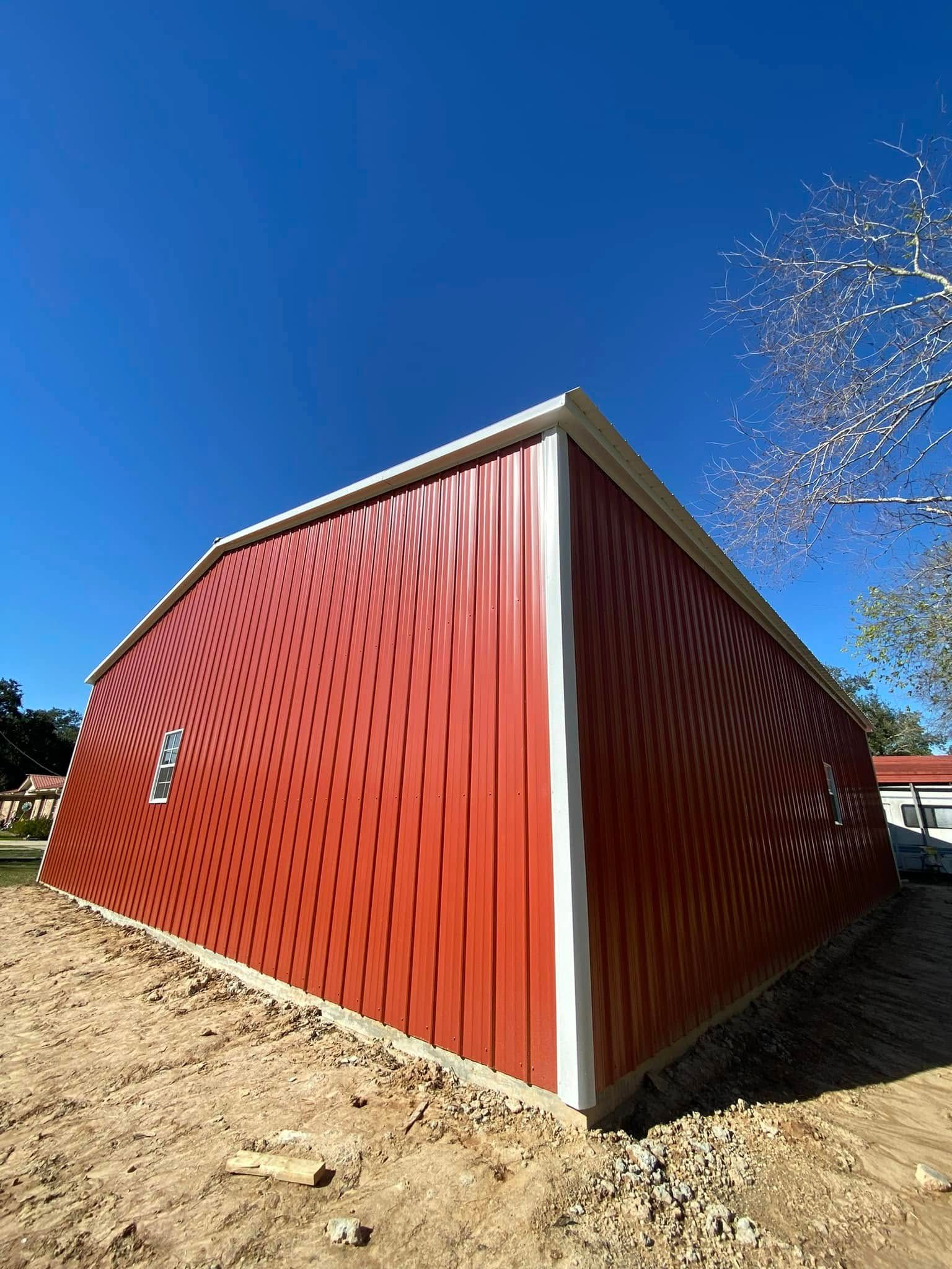A red barn with a white trim is sitting on top of a dirt field.