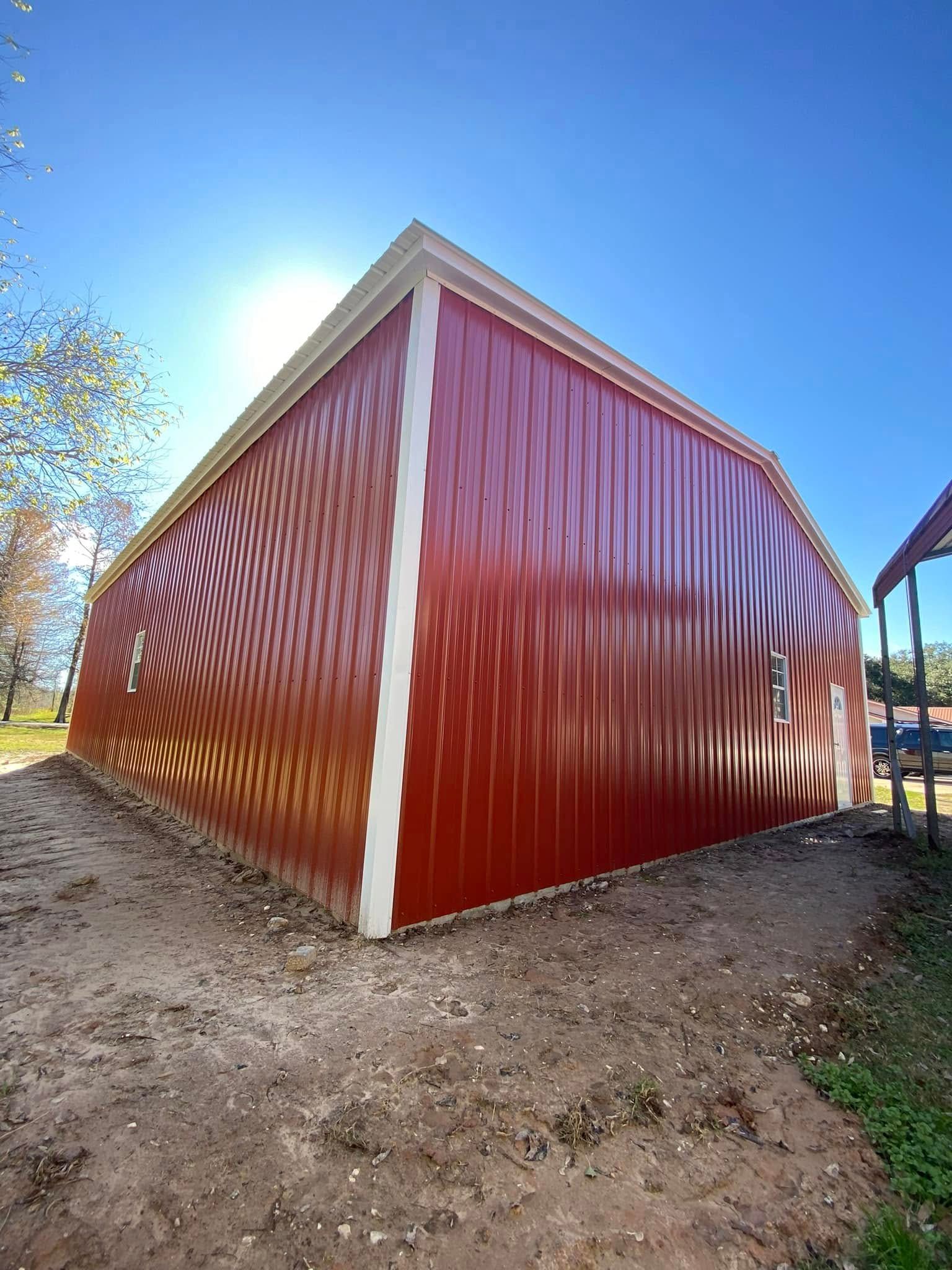 A red barn with a white trim is sitting on top of a dirt field.