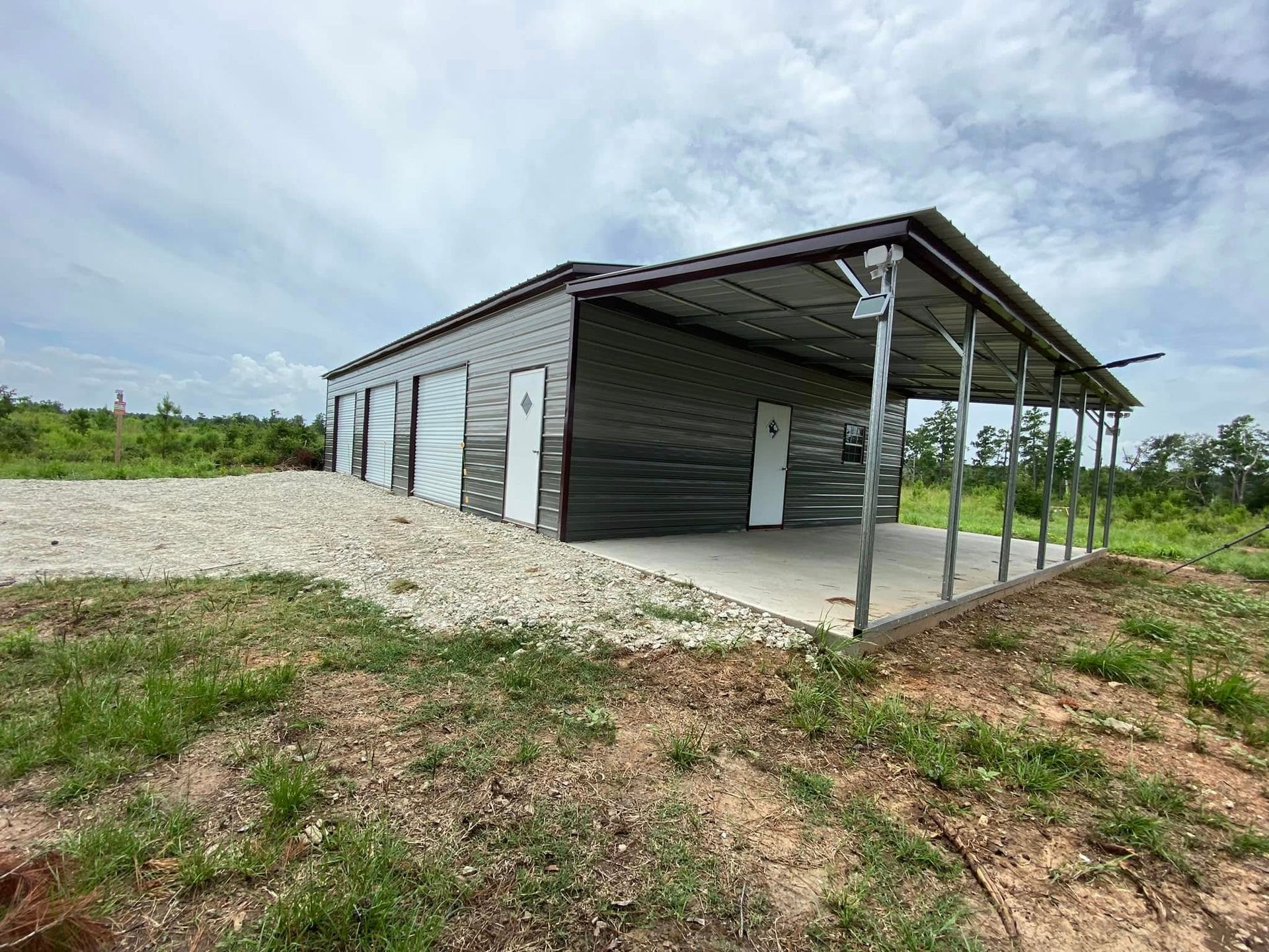 A large metal building with a porch is sitting in the middle of a grassy field.
