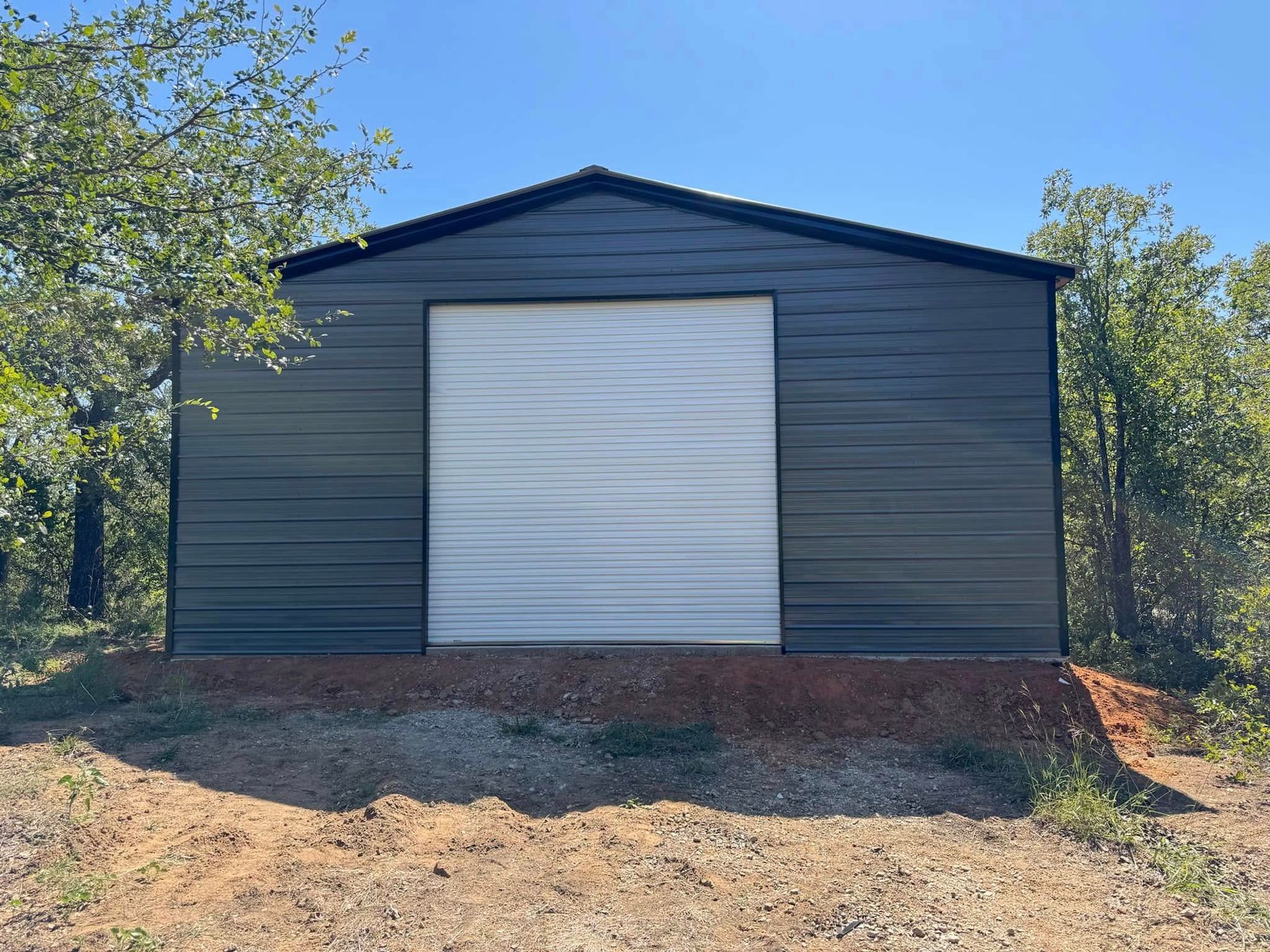 A black metal garage with a white garage door is sitting on top of a dirt hill.