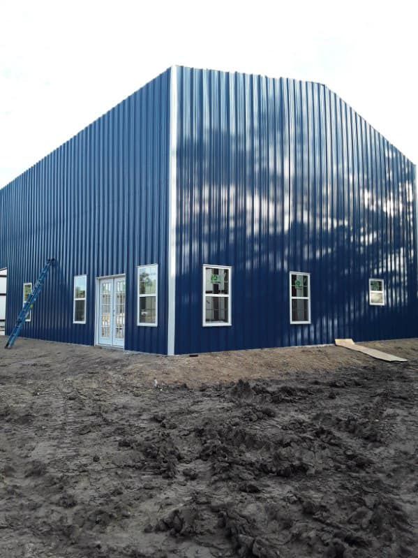 A large blue building with a ladder in the dirt in front of it.