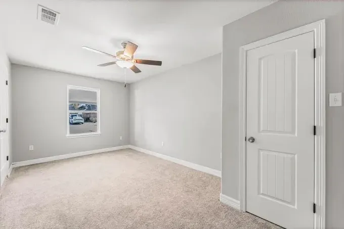 An empty bedroom with a ceiling fan and a window.